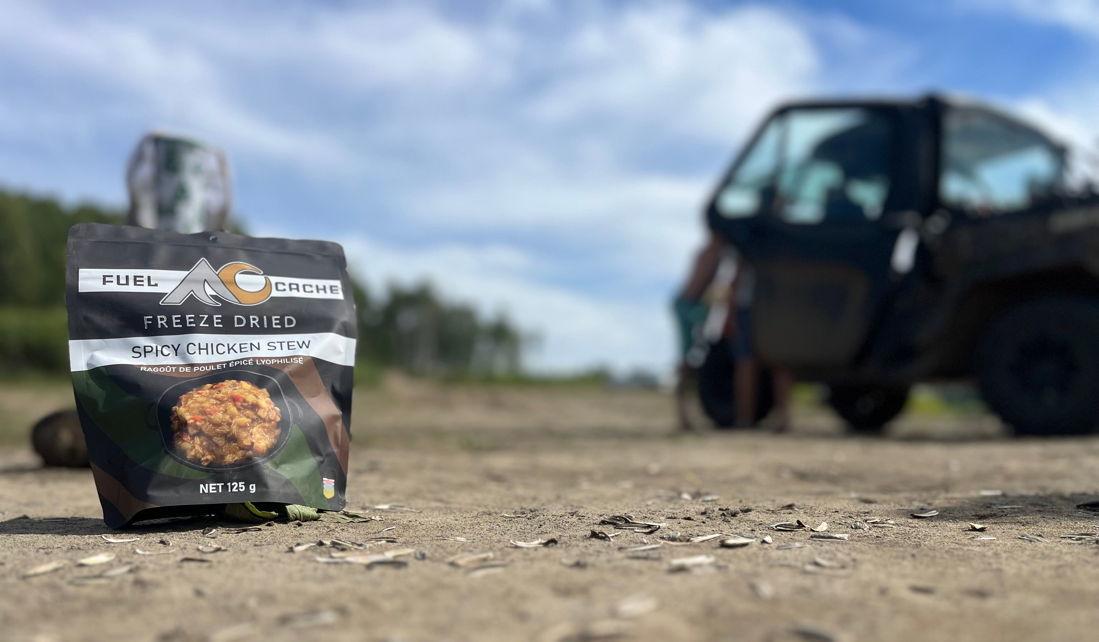 Fuel Cache freeze-dried spicy chicken stew package on a dirt road with a vehicle in the background